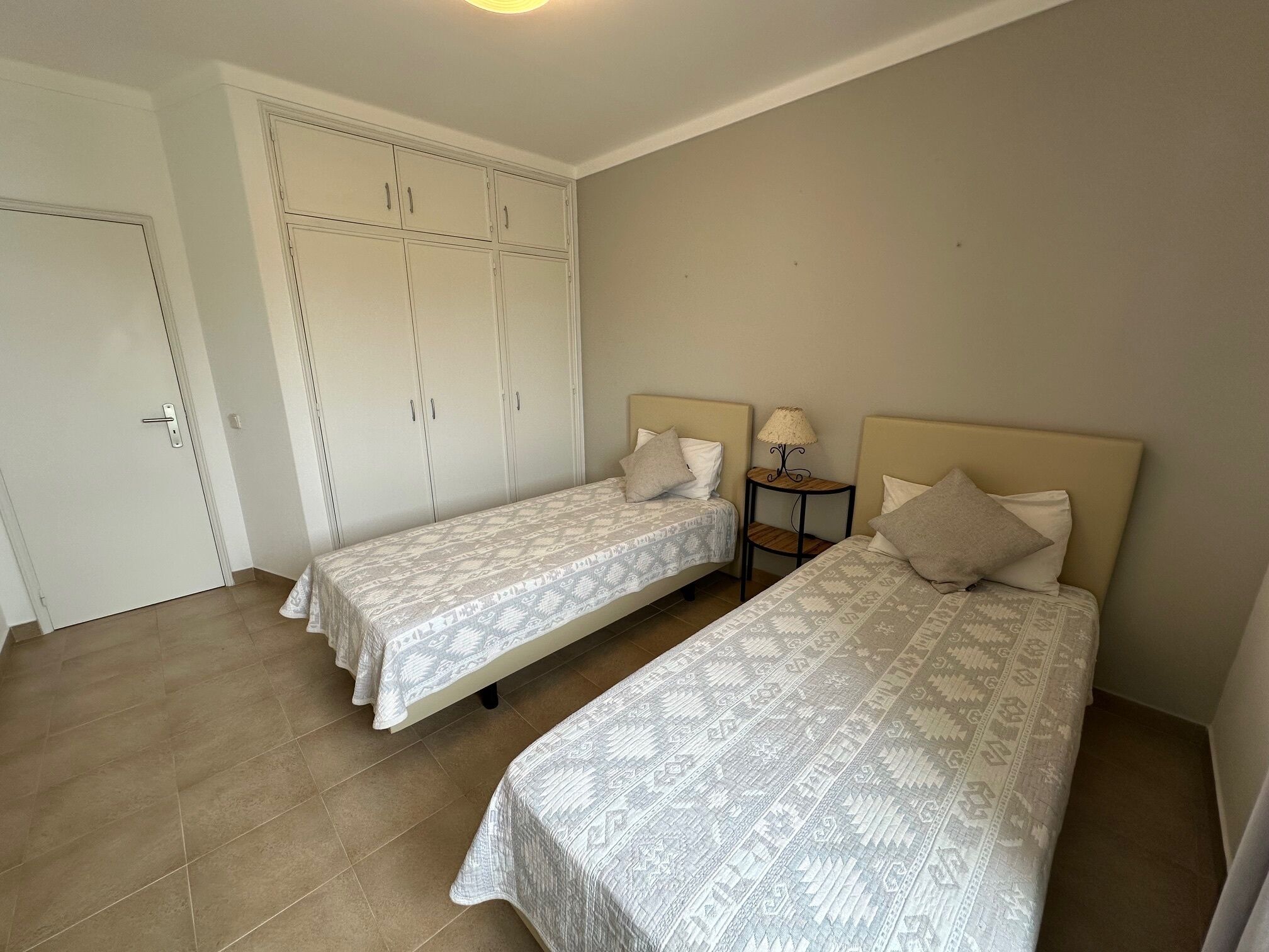 Un dormitorio con dos camas, un armario y una mesita de noche con lámpara.