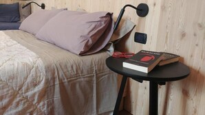 A bedroom with a bed, pillows, a bedside table with a book, and a wall-mounted lamp. - B&B Mirò (Pieve di Soligo)