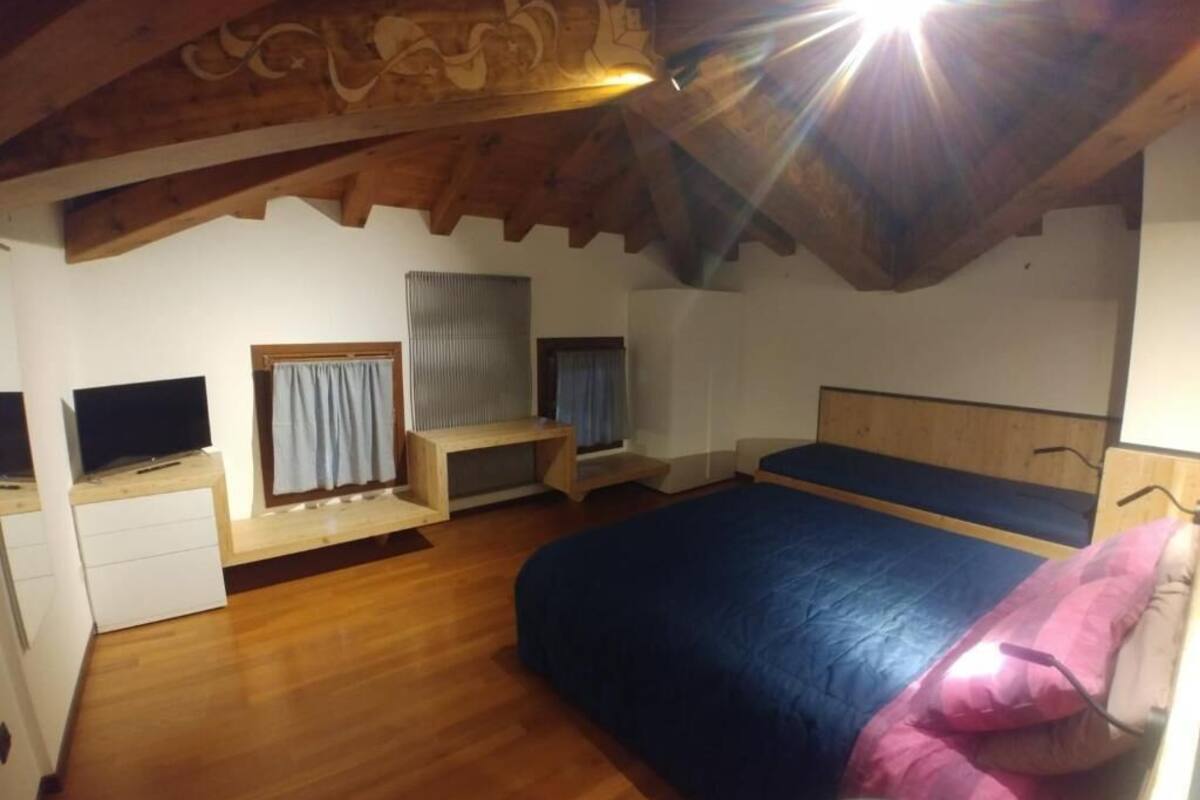 Ein Schlafzimmer mit einem Bett, einem Fernseher, einem Fenster mit Vorhängen und einer Holzbalkendecke.