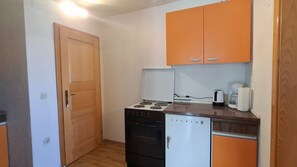 Eine kompakte Küche mit Herd, Backofen und Kühlschrank, Holzschränken und einer Tür.