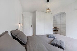 A bedroom with a bed, pillows, a hanging light fixture, a door, and a tiled wall.