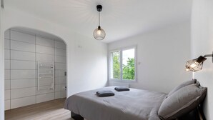 Un dormitorio con cama, ventana, radiador y lámpara colgante.