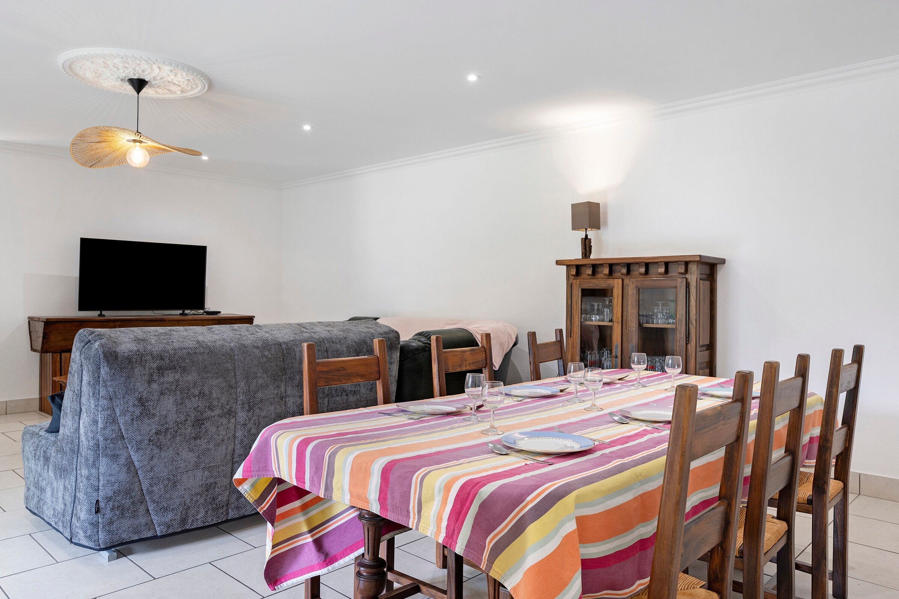 Un coin repas avec une nappe à rayures, des chaises en bois, un téléviseur et un meuble.