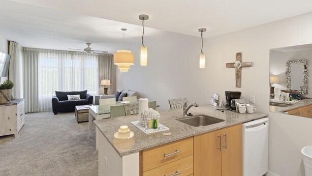 Eine moderne Küche mit Geschirrspüler, ein Essbereich mit Tisch und Stühlen sowie ein Wohnzimmer mit Sofa und Deckenventilator.