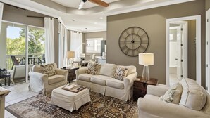 Un salón con ventilador de techo, un reloj de pared grande y vistas al exterior.