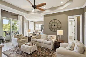A living room with a ceiling fan, a large wall clock, and a view of the outdoors. - 2 Bedroom Condo in Crystal Cove (Miramar Beach)