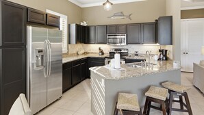 Cocina moderna con armarios oscuros, electrodomésticos de acero inoxidable, encimera de granito y decoración de pared con motivos marinos.