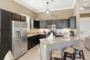 A modern kitchen with dark cabinets, stainless steel appliances, a granite countertop, and a fish-themed wall decoration. - 2 Bedroom Condo in Crystal Cove (Miramar Beach)