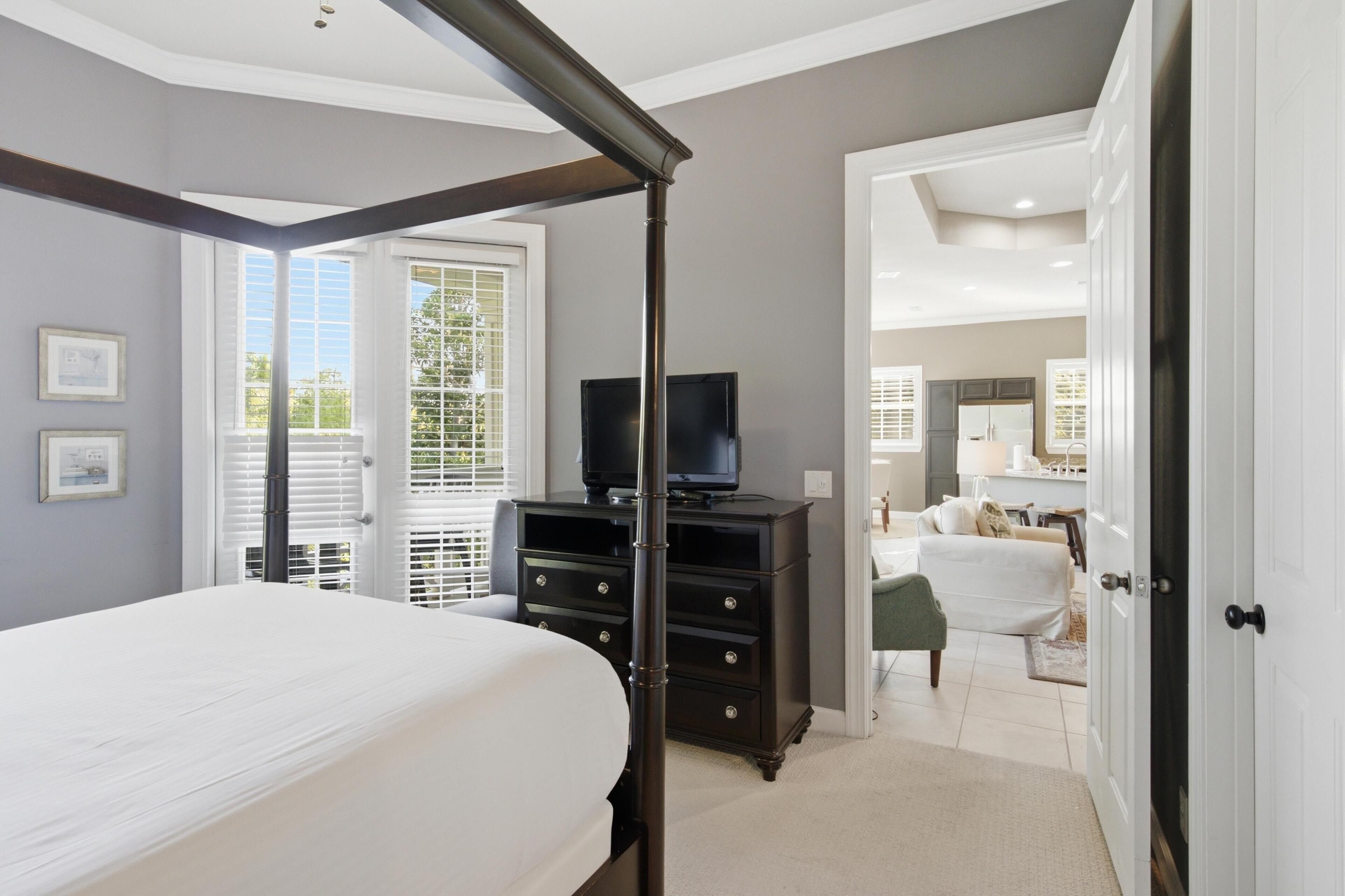 A bedroom with a bed, a dresser, a television, and a door leading to another room.