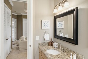 A bathroom with a granite countertop, a sink, a mirror, and two wall clocks. - 2 Bedroom Condo in Crystal Cove (Miramar Beach)