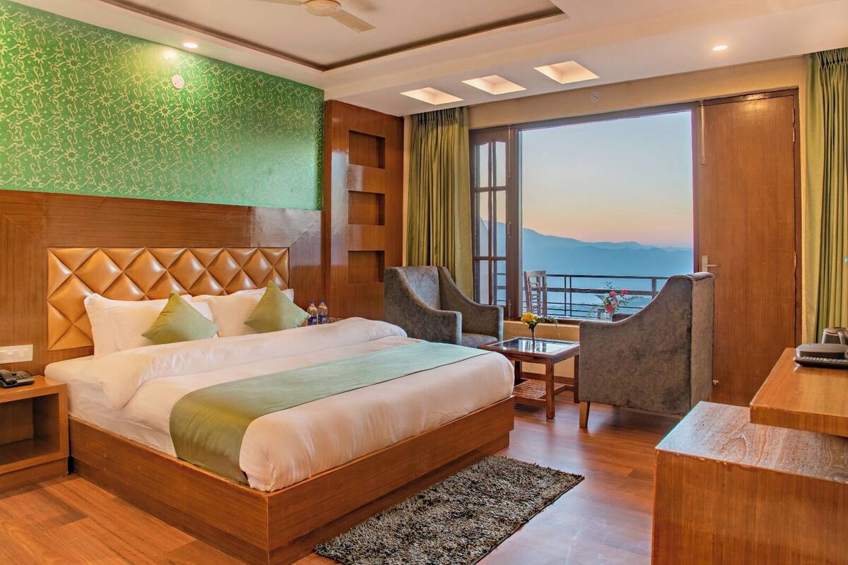 Ein Hotelzimmer mit einem großen Bett, einem Schreibtisch, zwei Stühlen und Blick auf das Meer, sowie einer grünen Wand.