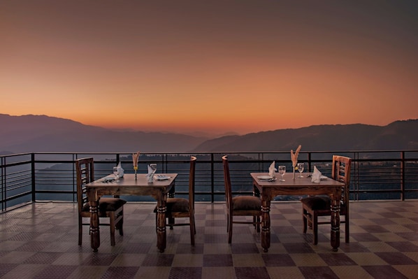 A dining area with tables and chairs, a checkered floor, and a scenic mountain view.