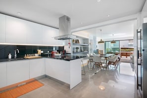 A modern kitchen with a central island, built-in appliances, and a dining area with a glass partition. - Villa 'Meluna' with Balcony, Wi-Fi and Air Conditioning (Albufeira)