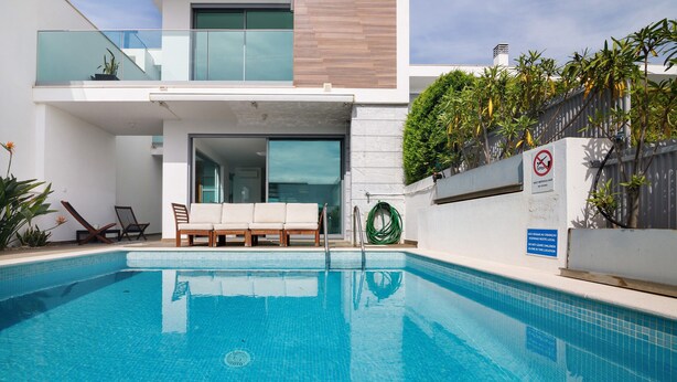 Ein moderner Poolbereich mit klarem, blauem Wasser, einer Liege, einer Couch und einem Glasgeländer.