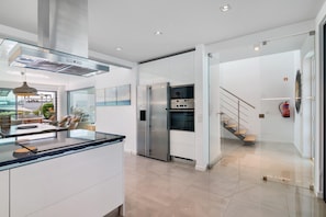 A modern kitchen with a glass island, stainless steel appliances, and a view to the outdoors. - Villa 'Meluna' with Balcony, Wi-Fi and Air Conditioning (Albufeira)