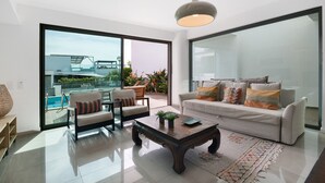 Ein modernes Wohnzimmer mit einer Couch, Sesseln, einem Couchtisch und einer großen Glastür, die auf einen Balkon mit einem Pool führt.