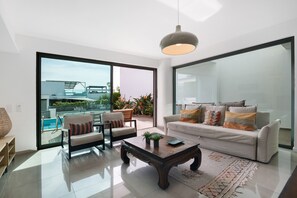 A modern living room with a sofa, armchairs, a coffee table, and a large glass door leading to a balcony with a pool. - Villa 'Meluna' with Balcony, Wi-Fi and Air Conditioning (Albufeira)