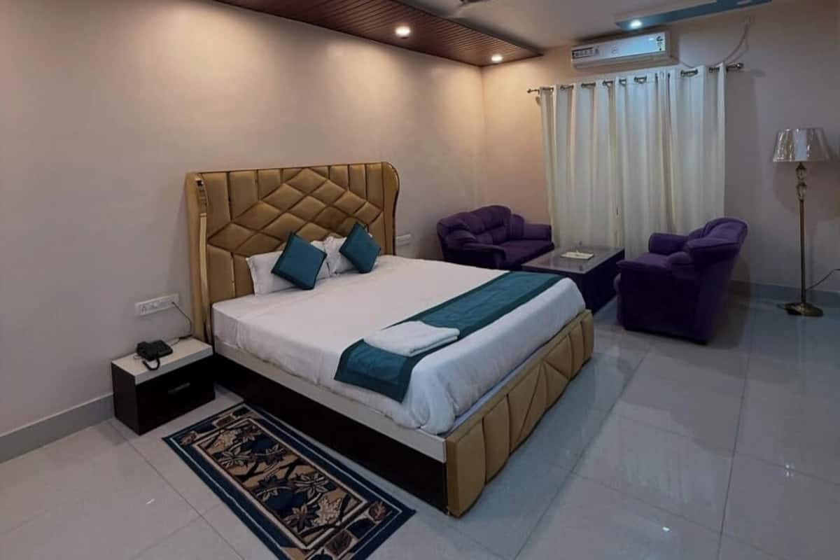 Ein Schlafzimmer mit einem großen Bett, zwei violetten Sesseln, einem kleinen Tisch, einer Stehlampe und einem Deckenventilator.