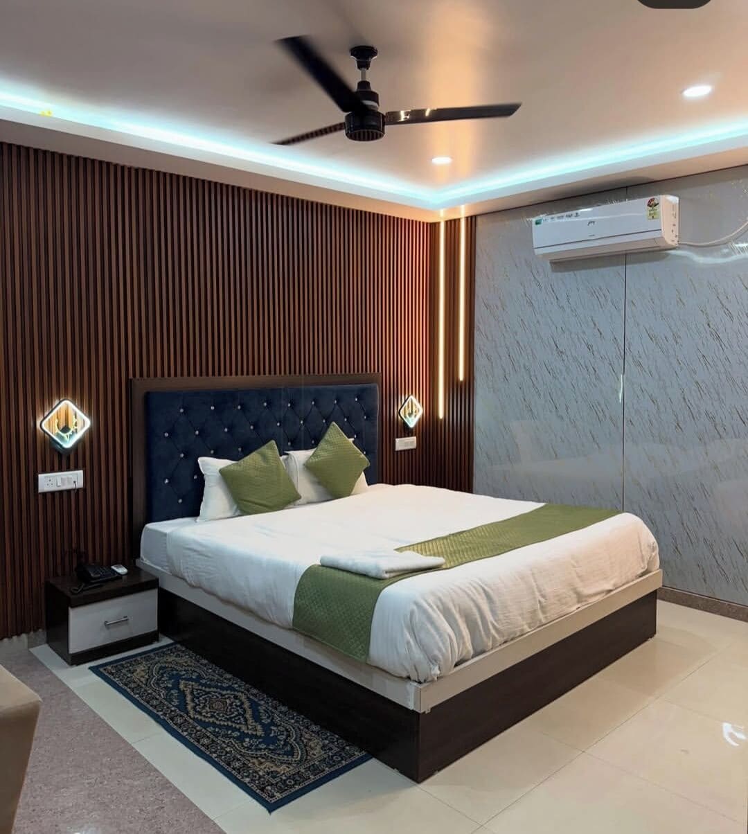 Un dormitorio moderno con cabecera capitonada, cama con sábanas blancas, un plaid verde, un ventilador de pie y aire acondicionado de pared.