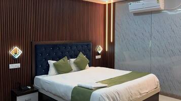 Un dormitorio moderno con cabecera capitonada, cama con sábanas blancas, un plaid verde, un ventilador de pie y aire acondicionado de pared.