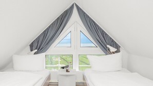 Une chambre avec deux lits, une table de chevet blanche, une lampe et une fenêtre avec des rideaux.