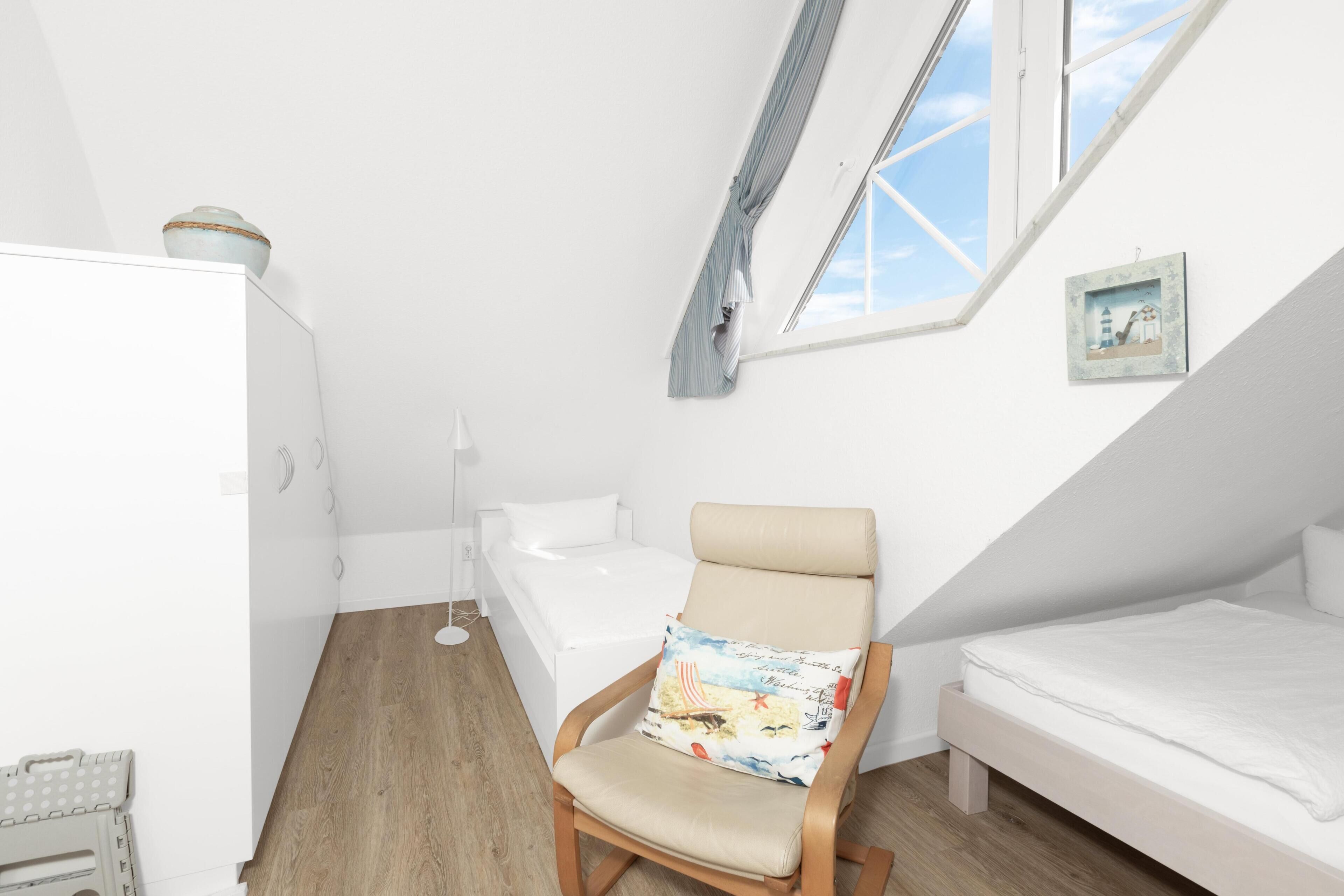 Une petite pièce lumineuse, avec un lit en mezzanine, une chaise avec un coussin, une petite table et une fenêtre donnant sur un beau paysage.