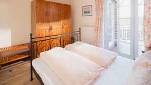 A bedroom with a bed, wooden wardrobe, and a window with curtains. - "Dünenblick" at Haus Sanderling - your vacation paradise with a view (Juist)