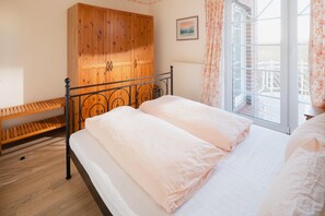 A bedroom with a bed, wooden wardrobe, and a window with curtains. - "Dünenblick" at Haus Sanderling - your vacation paradise with a view (Juist)