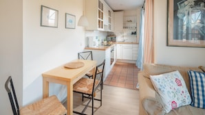 A compact kitchen with a dining area, a sofa with decorative pillows, and a framed artwork on the wall. - "Dünenblick" at Haus Sanderling - your vacation paradise with a view (Juist)