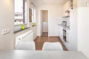 Eine moderne Küche mit weißen Schränken, einem eingebauten Backofen und einem Fenster mit Blick auf Gebäude.