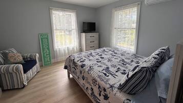 A bedroom with a bed, a chair, a dresser, a television, and a ceiling fan.