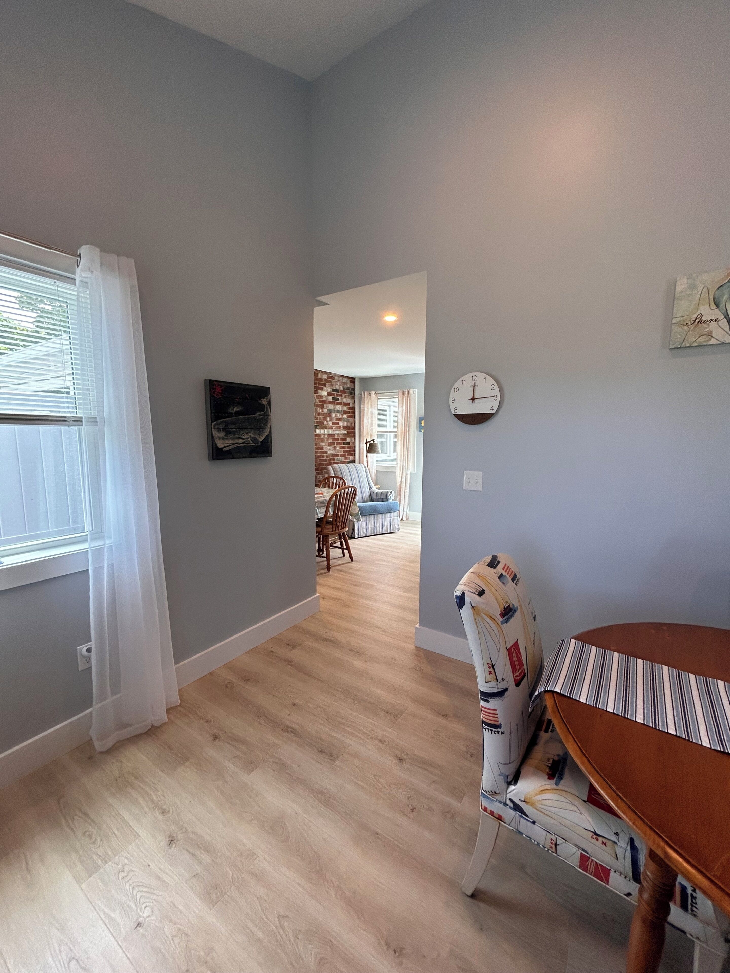 A room with a dining table, a clock on the wall, and a view into another room with a dining table and chairs.