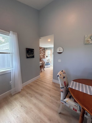 A room with a dining table, a clock on the wall, and a view into another room with a dining table and chairs.