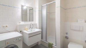 Een moderne badkamer met een wasmachine, wastafel, spiegel, douche en toilet.