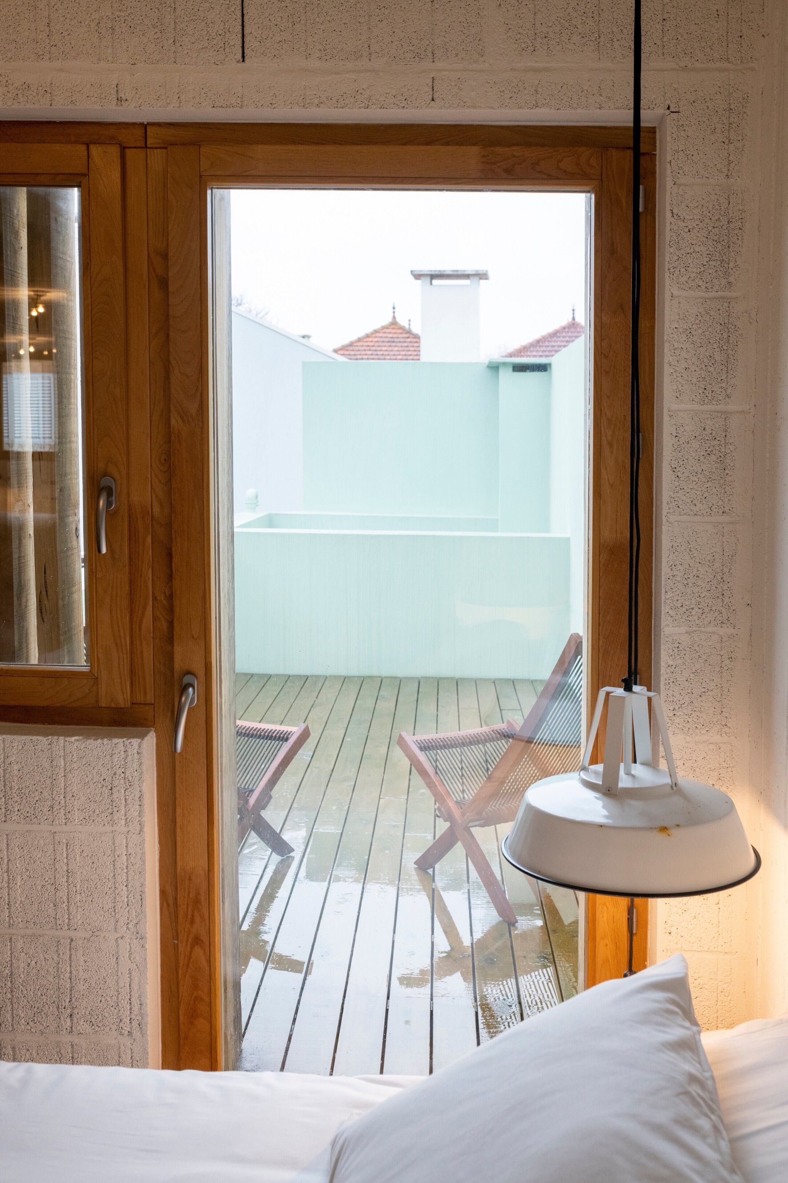 Een kamer met een houten deur die leidt naar een balkon met een witte stoel en een tafellamp.