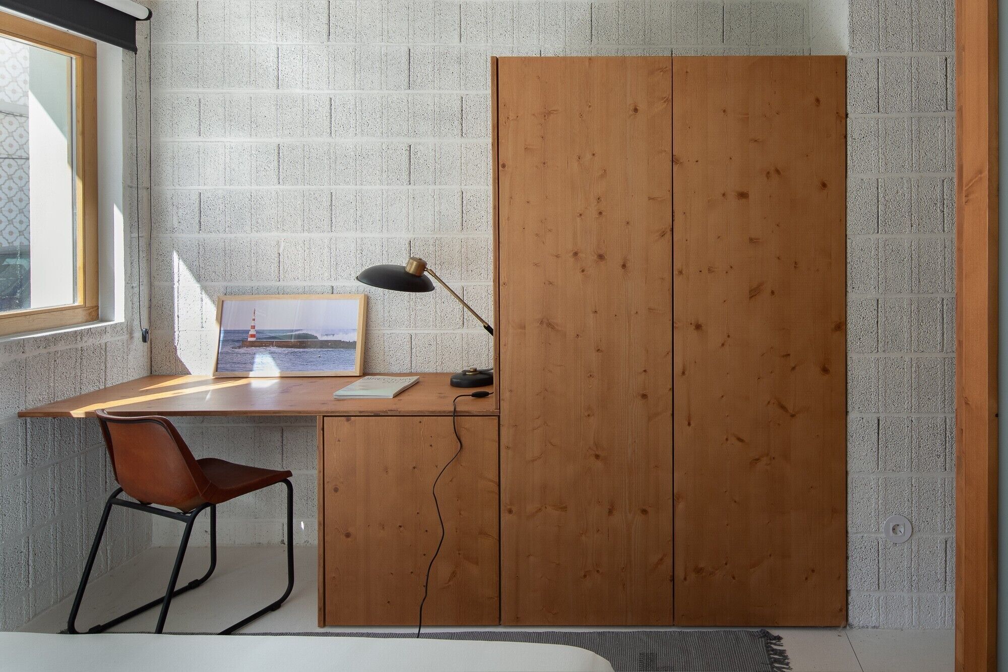 Una habitación con escritorio de madera, una silla, una lámpara y un armario.