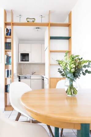 Eine moderne Küche mit weißen Schränken, einem eingebauten Backofen und einem Essbereich mit Holztisch und weißen Stühlen.