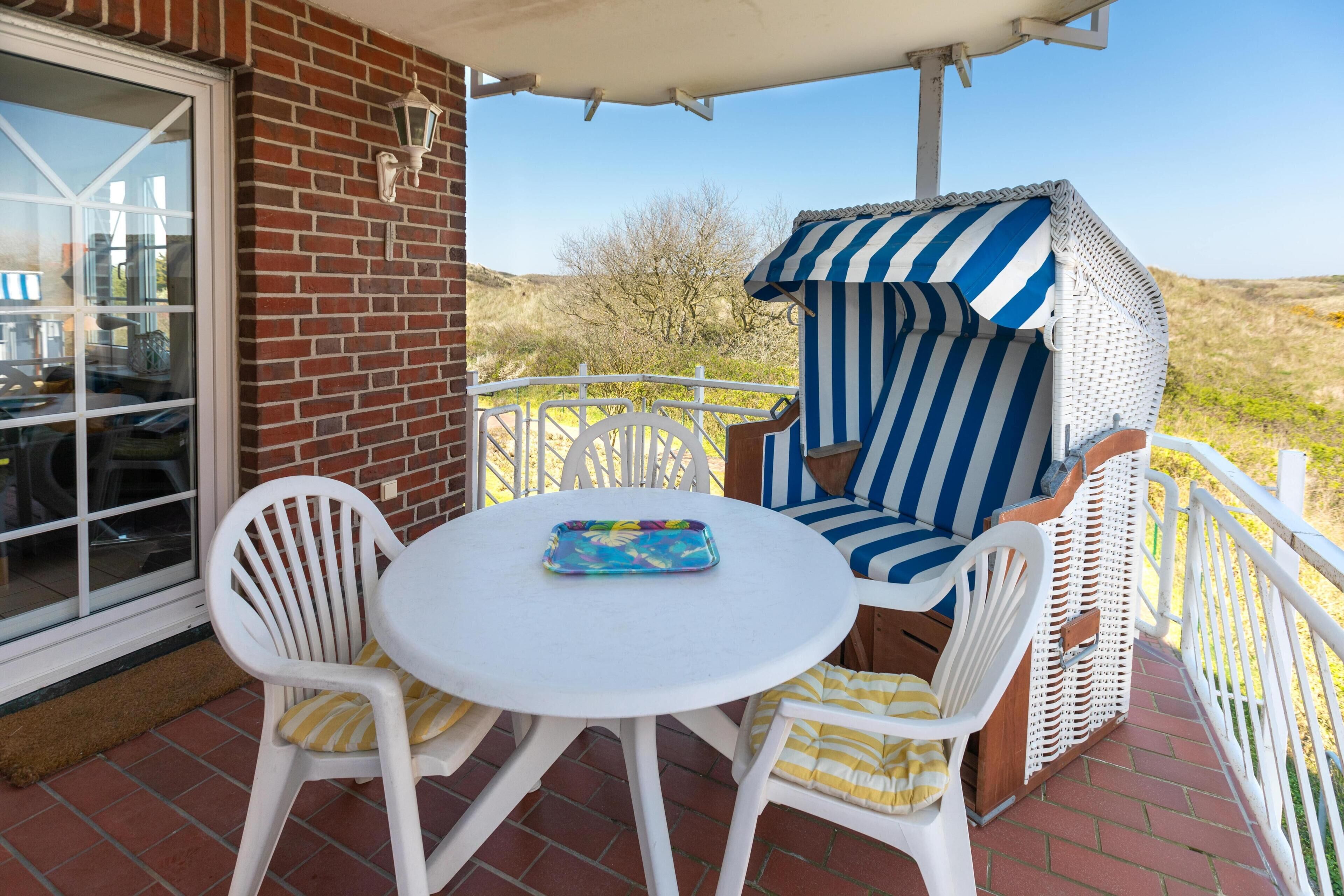 A patio with a round table and white chairs, a striped outdoor seating area, and a brick wall.