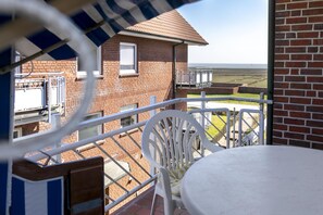 Ein Balkon mit Tisch und Stühlen, der auf ein Backsteingebäude und den Blick aufs Meer blickt.