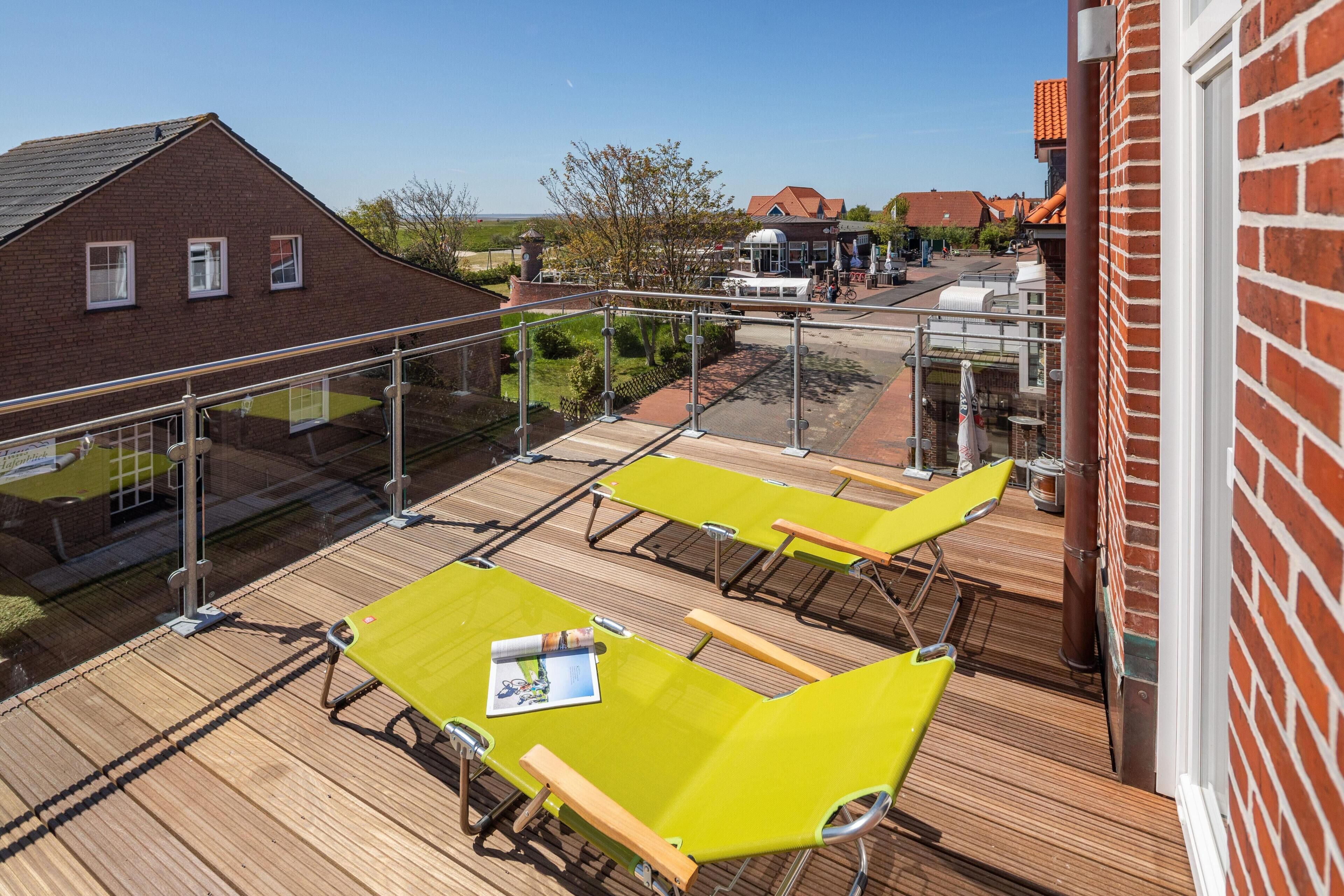 Een terras op het dak met gele stoelen en een tafel, met uitzicht op een woongebied met bakstenen gebouwen en een heldere lucht.