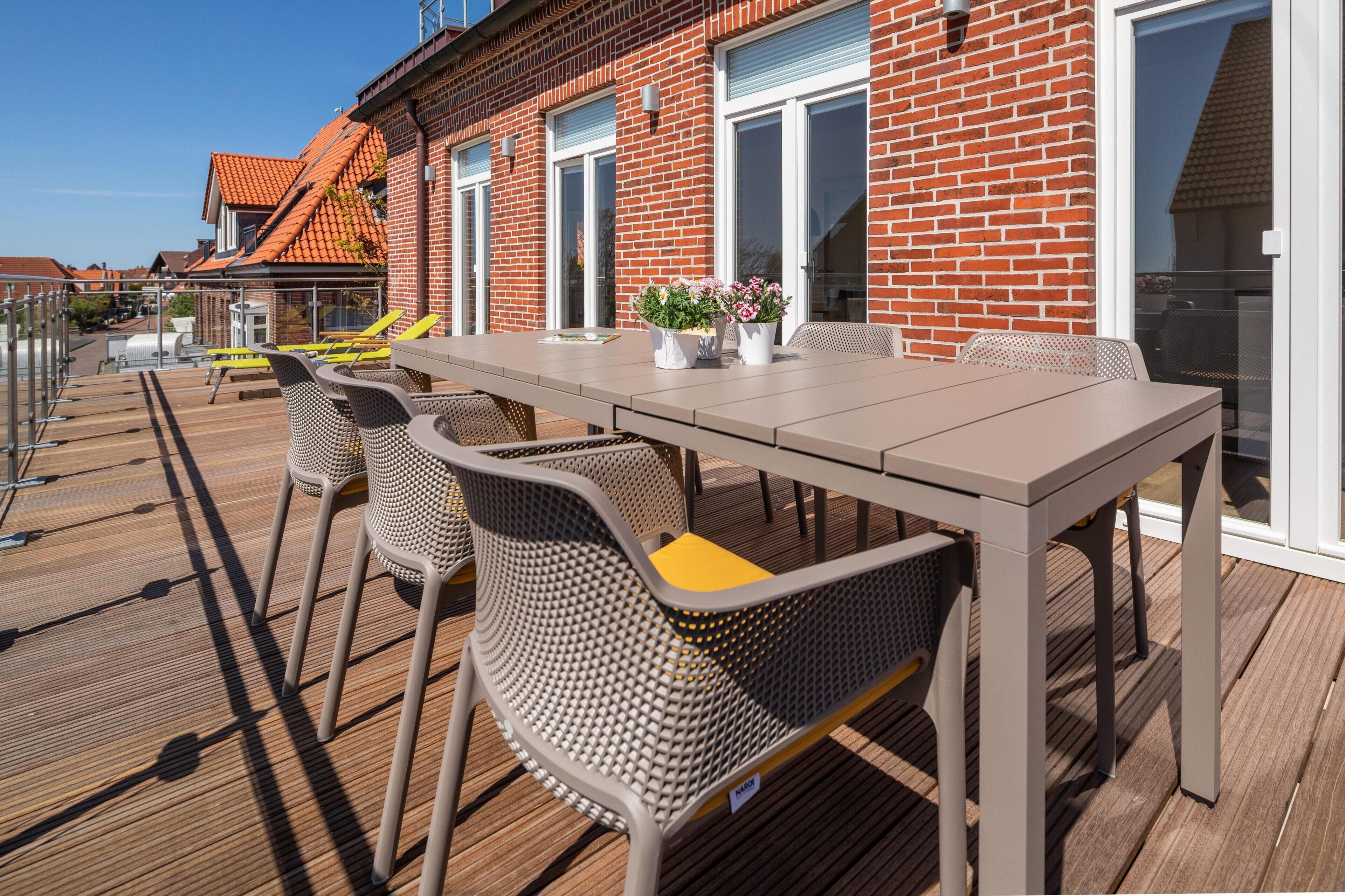 An outdoor dining area with a table and chairs, a brick building with large windows, and a clear sky.