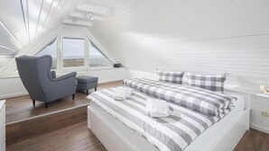 Ett sovrum med en säng, en stol, ett litet bord, ett fönster med utsikt och ett takfönster.