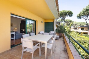 Un patio con una mesa y sillas blancas, un sofá y una puerta corredera que da a un espacio interior.