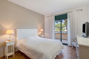 Un dormitorio con cama, dos lámparas de noche, televisión y balcón con cortinas.