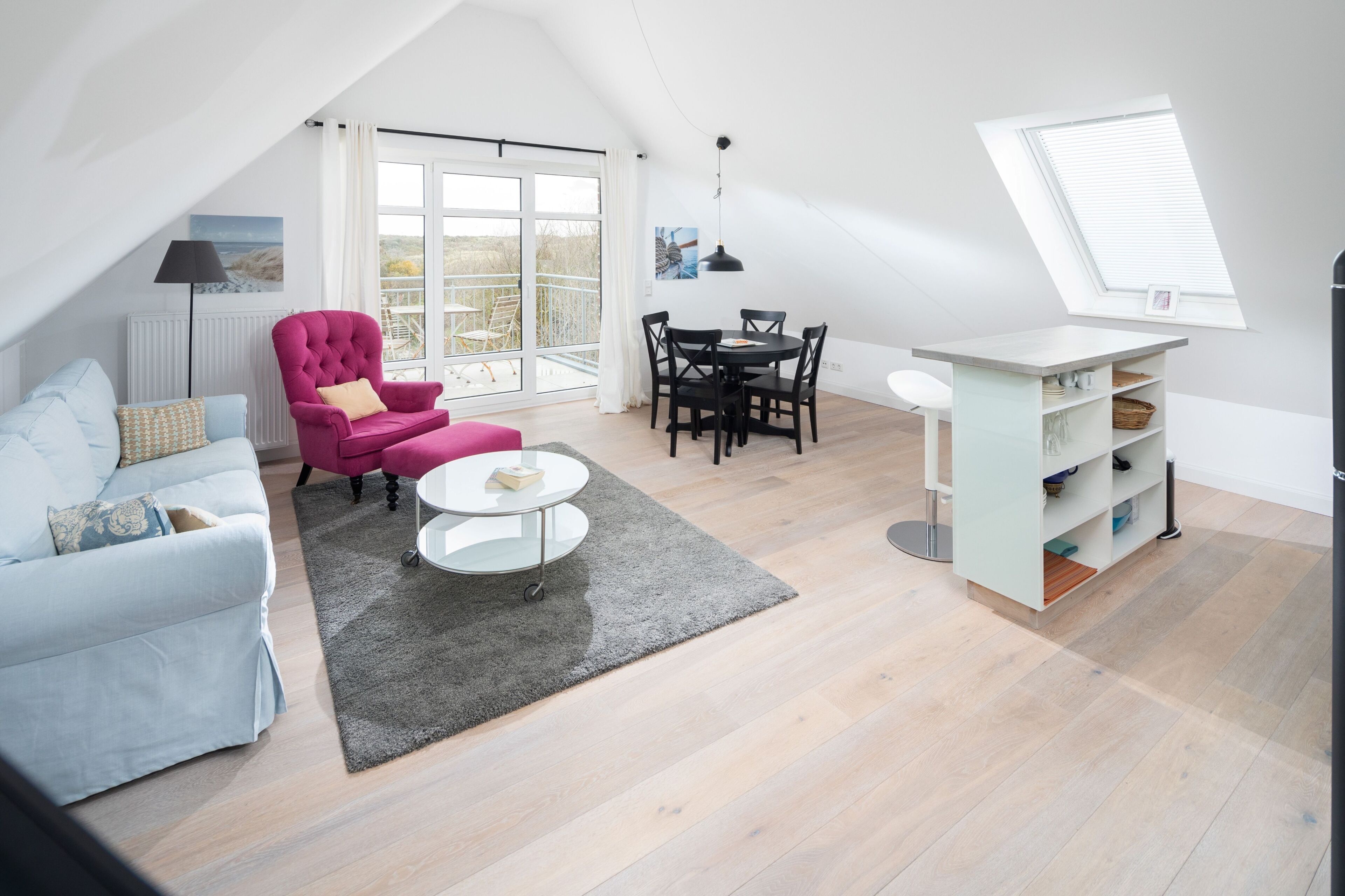 A modern loft apartment with a dining area, a pink armchair, a white sofa, and a large window.