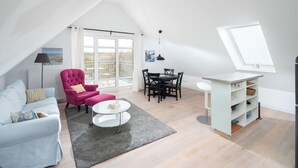Een modern loft appartement met een eethoek, een roze fauteuil, een witte bank en een groot raam.