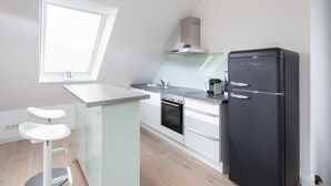 Een moderne keuken met een zwarte koelkast, witte kasten, een inbouwoven en een klein eiland met barkrukken.