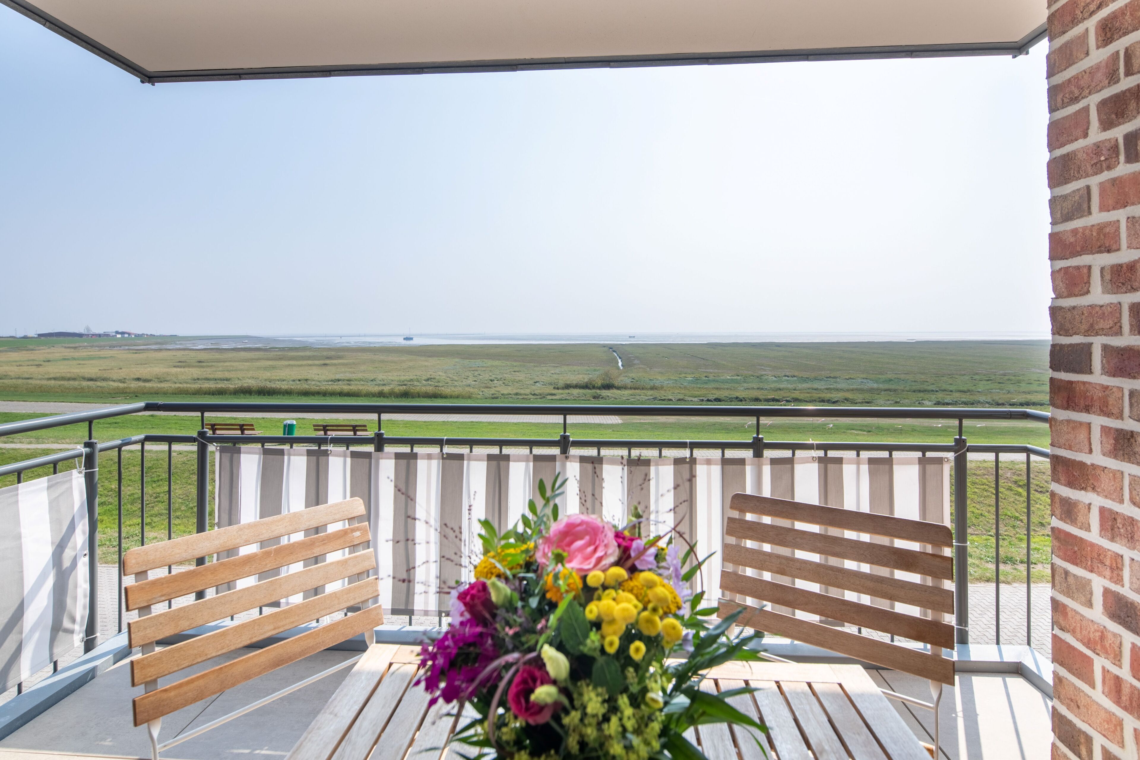 En balkon med to træbænke, en blomsteropsætning og udsigt til havet.