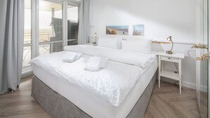 Habitación de hotel con una cama grande, una mesita de noche con lámpara, una pequeña mesita auxiliar y vistas al exterior.