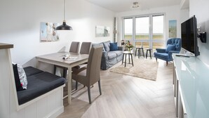 Una sala de estar moderna con comedor, un sofá, un televisor y vistas amplias a través de grandes ventanales.